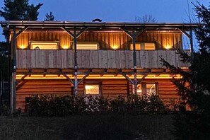 A two-story wooden cabin with a balcony on the upper level, surrounded by vegetation. - Holiday home in the Harz Mountains with 2 bedrooms (Harzgerode OT Güntersberge)