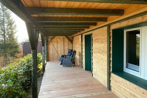 A wooden cabin with a covered porch, a chair, and a window. - Holiday home in the Harz Mountains with 2 bedrooms (Harzgerode OT Güntersberge)