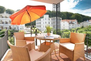 A balcony with wicker furniture, a table with a magazine, and an orange umbrella. - Villa Lena Apt. 7, Nagel Family (Sellin)