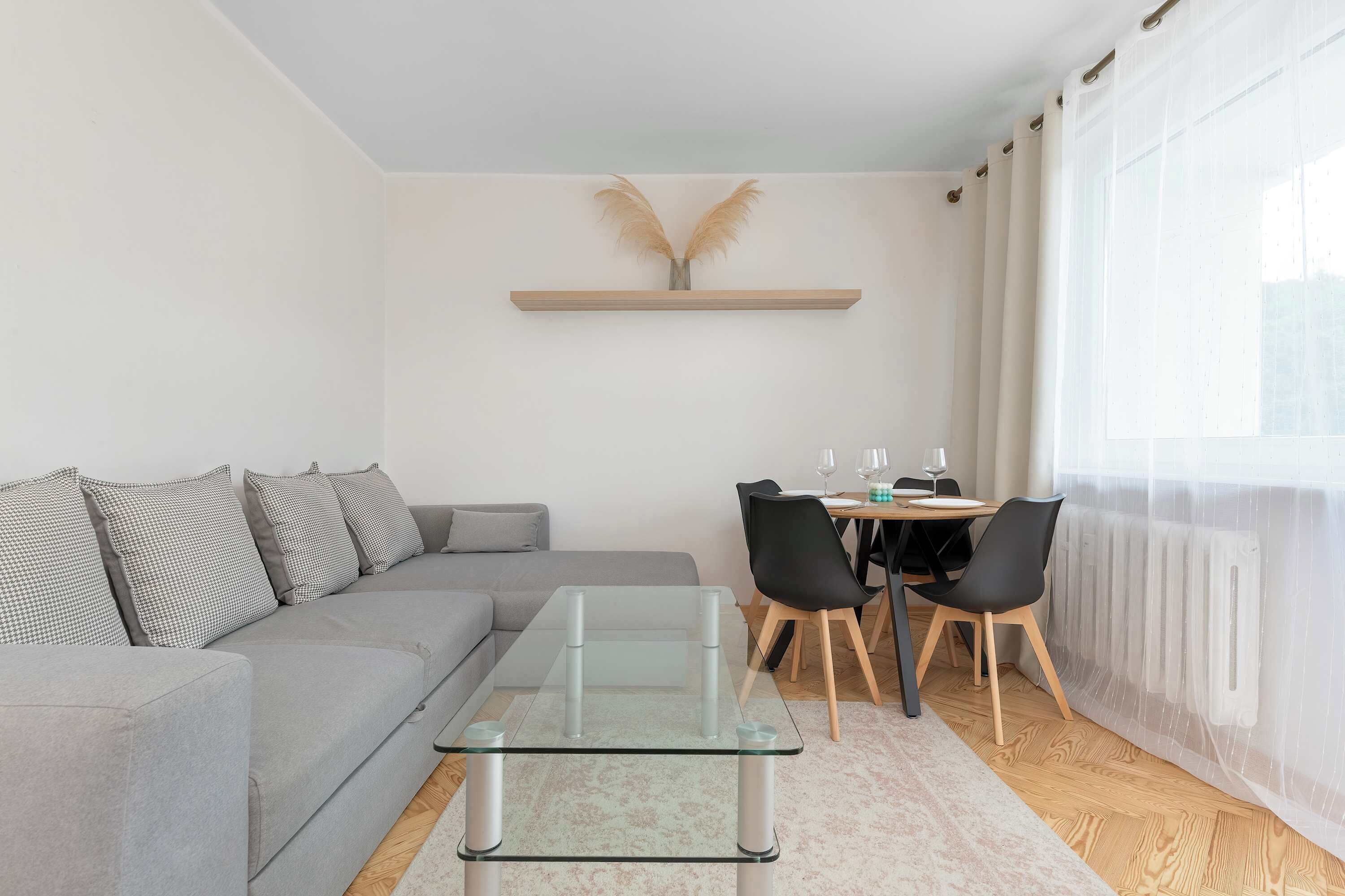 Una sala de estar moderna con un sofá gris, una mesa de centro de vidrio y un comedor con mesa de madera y sillas negras.