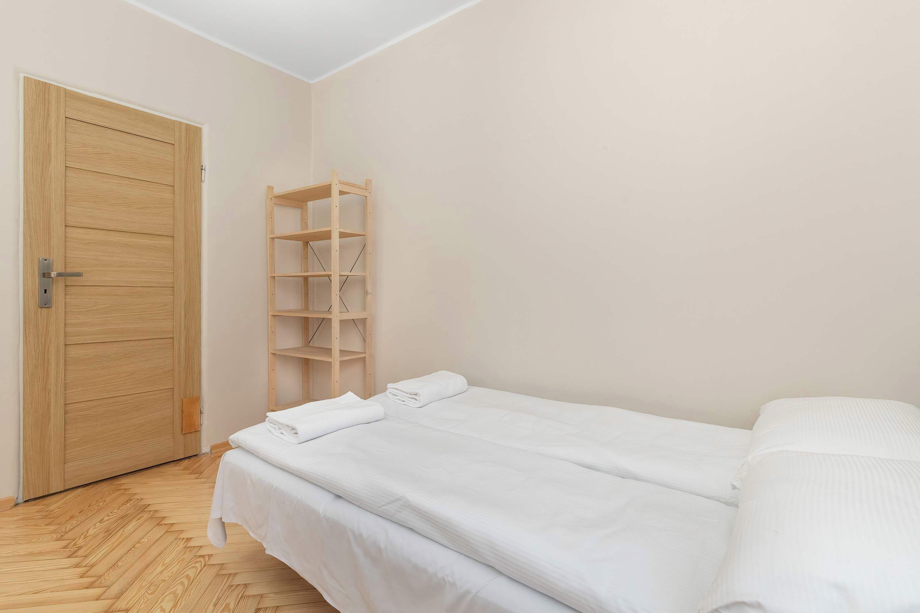 Ein Zimmer mit Holztür, einer Holzregaleinheit und einem Bett mit weißer Bettwäsche.