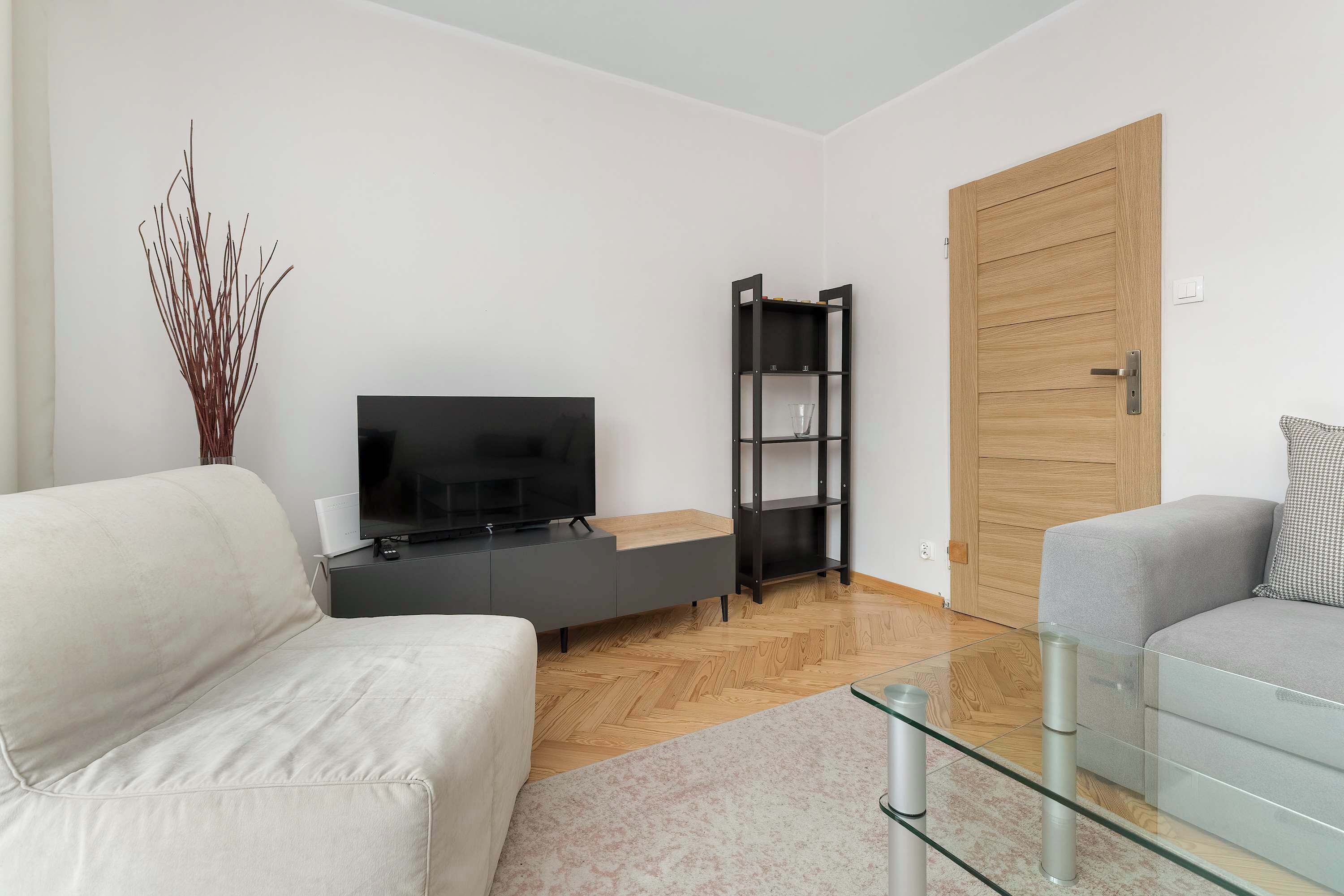 A modern living room with a flat-screen TV, a black shelving unit, a wooden door, and two sofas.