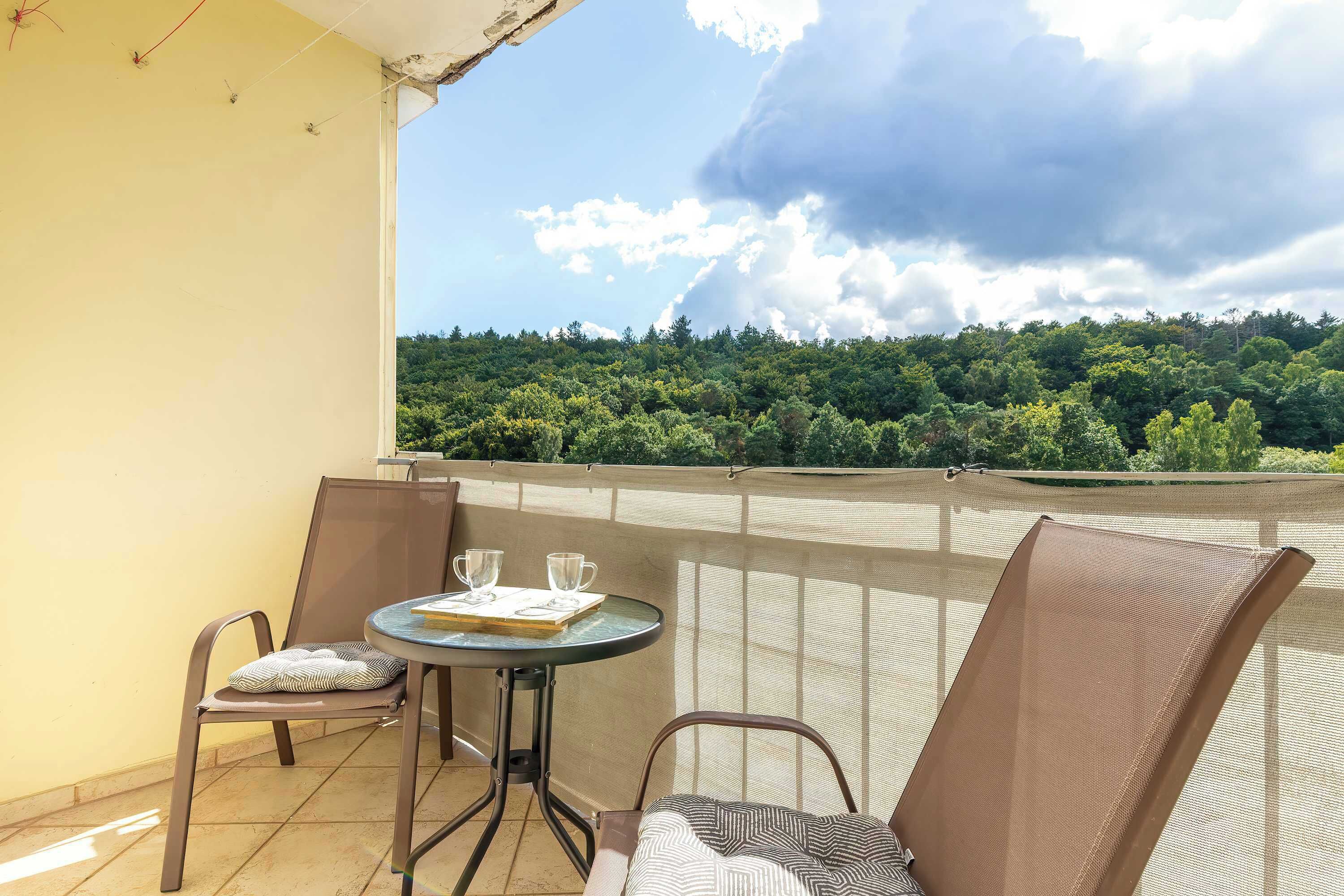 Un balcón con mesa y sillas, con vista a una zona boscosa.