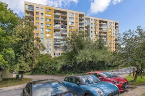 Un edificio residencial de varios pisos con balcones, coches estacionados y árboles.