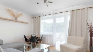 Een moderne woonkamer met een glazen salontafel, een bank, een eethoek met stoelen en uitzicht door grote ramen.