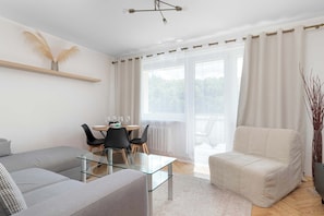 Una sala de estar moderna con una mesa de centro de vidrio, un sofá, un comedor con sillas y vistas amplias a través de grandes ventanas.