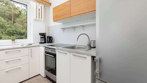 Een moderne keuken met witte kasten, een roestvrijstalen koelkast, een inbouwoven en een raam met uitzicht op groen.