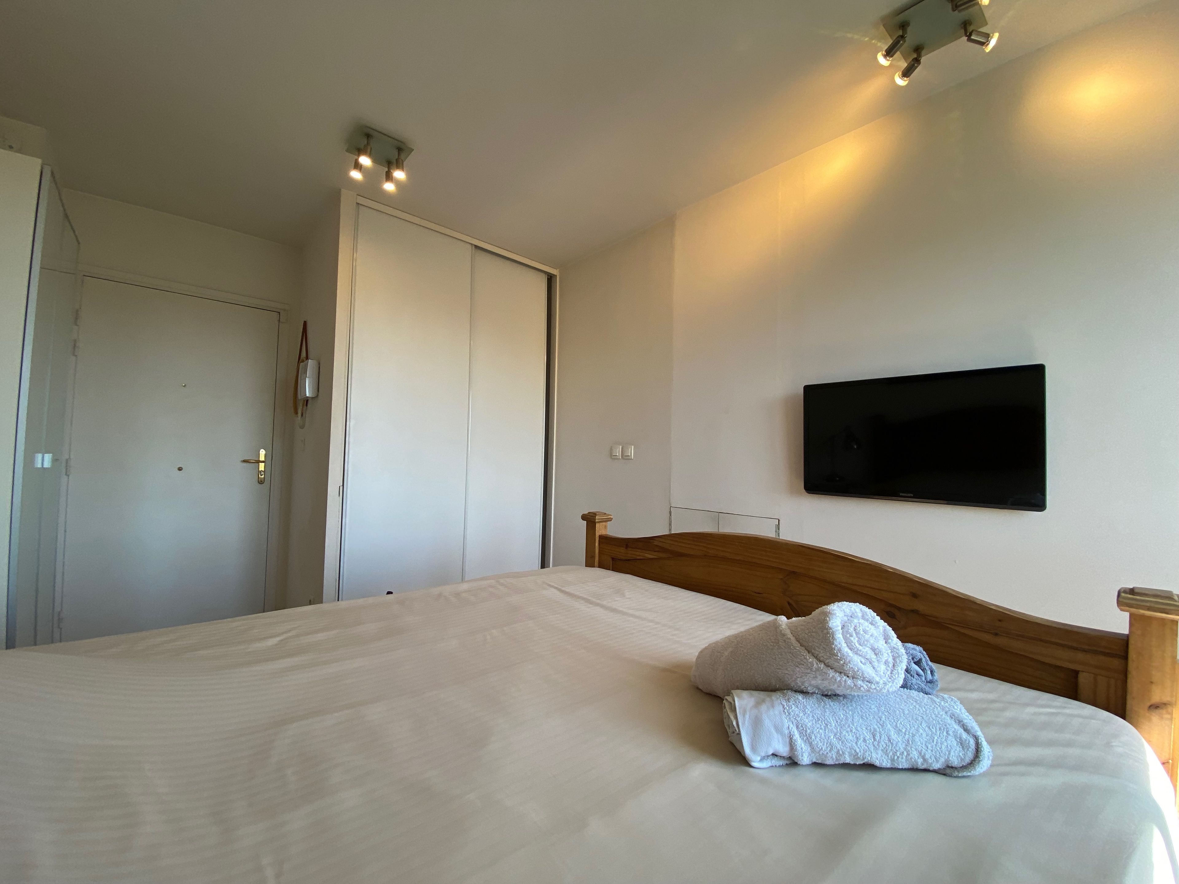 Ein Hotelzimmer mit einem Bett, einem an der Wand befestigten Fernseher und einer Tür mit Lichtschalter.