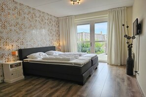 Ein Schlafzimmer mit einem großen Bett, einem Nachttisch, einem an der Wand befestigten Fernseher und Blick ins Freie.