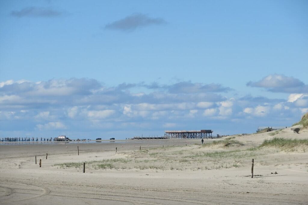 A beach with a pier structure, sandy dunes, and a clear sky.