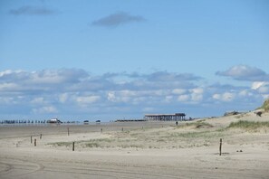 Ein Strand mit einem Steg, sandigen Dünen und blauem Himmel.