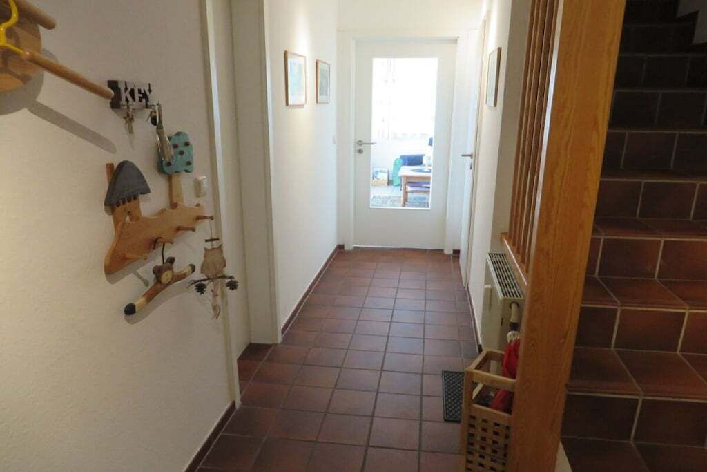 Ein Korridor mit gefliestem Boden, einer Holztür am Ende und einer Treppe zur rechten Seite.