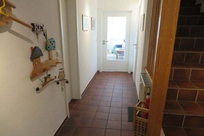 Ein Korridor mit gefliestem Boden, einer Holztür am Ende und einer Treppe zur rechten Seite.