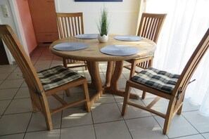 Ein runder Holzesstisch mit vier Stühlen, jeder mit Sitzkissen in Karomuster. Auf dem Tisch steht ein kleiner Topfpflanze.