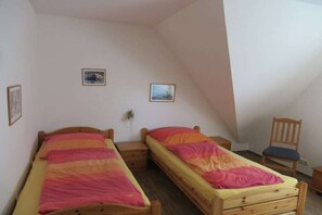 Una stanza con due letti di legno, una sedia in legno e un piccolo tavolo.