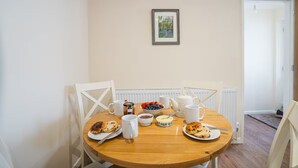 Una tavola da pranzo con prodotti per la colazione, sedie, un termosifone e un quadro appeso al muro.