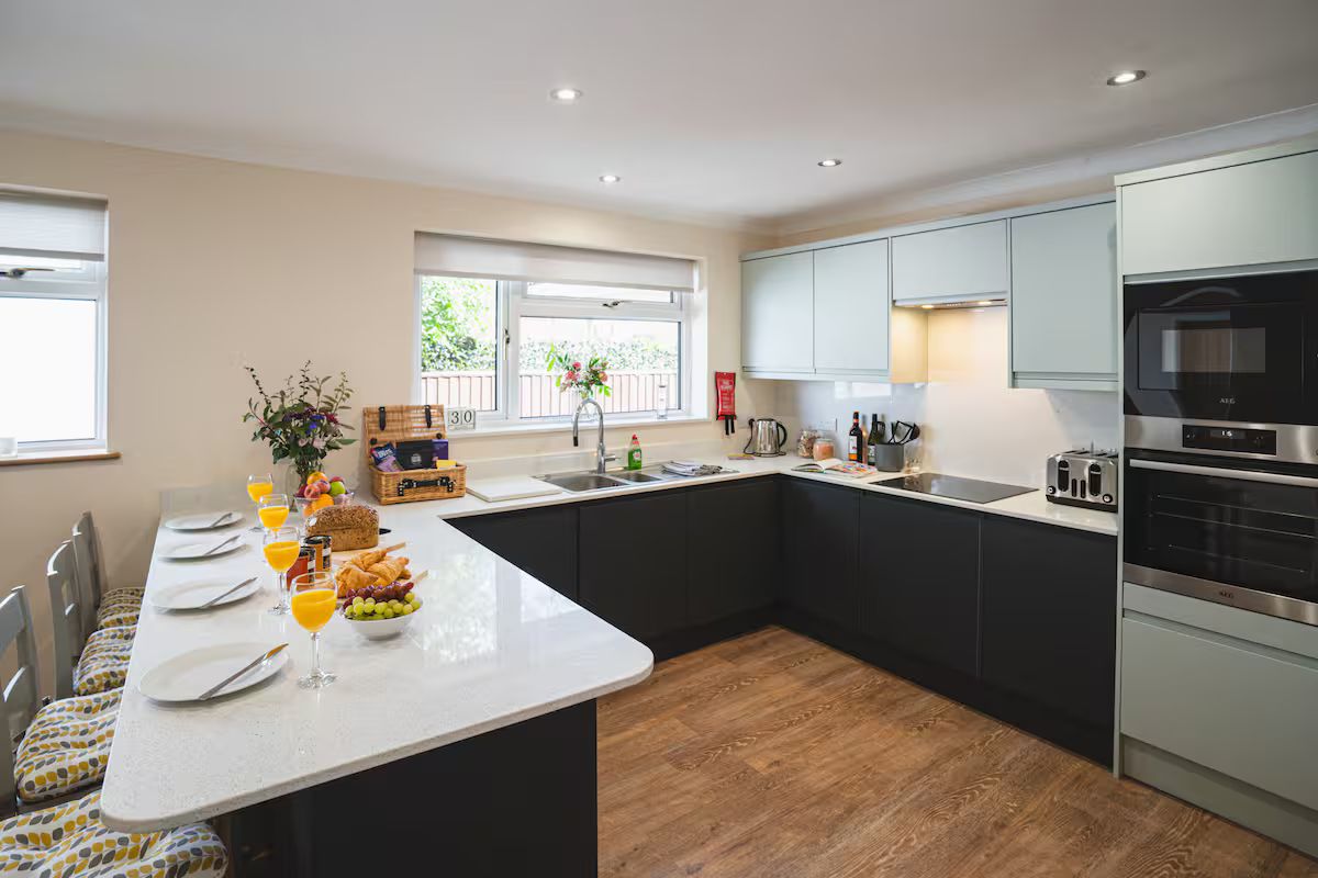 A modern kitchen with a central island, a built-in oven, and a window with a view of greenery.