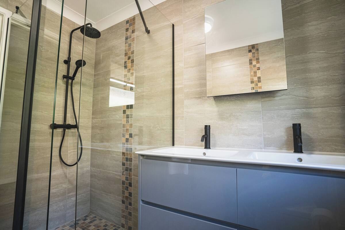 Un baño moderno con cabina de ducha, lavamanos con espejo y paredes con azulejos.