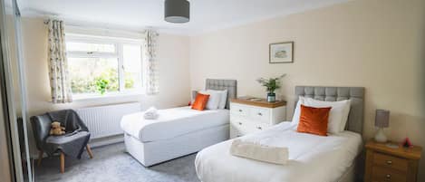 A bedroom with two beds, a chair, a bedside table, and a window with curtains.