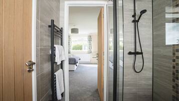 A modern bathroom with a glass shower enclosure, a towel rack with white towels, and a visible bedroom with a bed and a window.