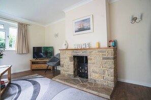 A living room with a stone fireplace, a television, a bookshelf, and a window with curtains.