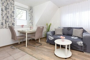Een moderne woonkamer met een bank, twee stoelen, een klein rond tafeltje en een raam met gordijnen.