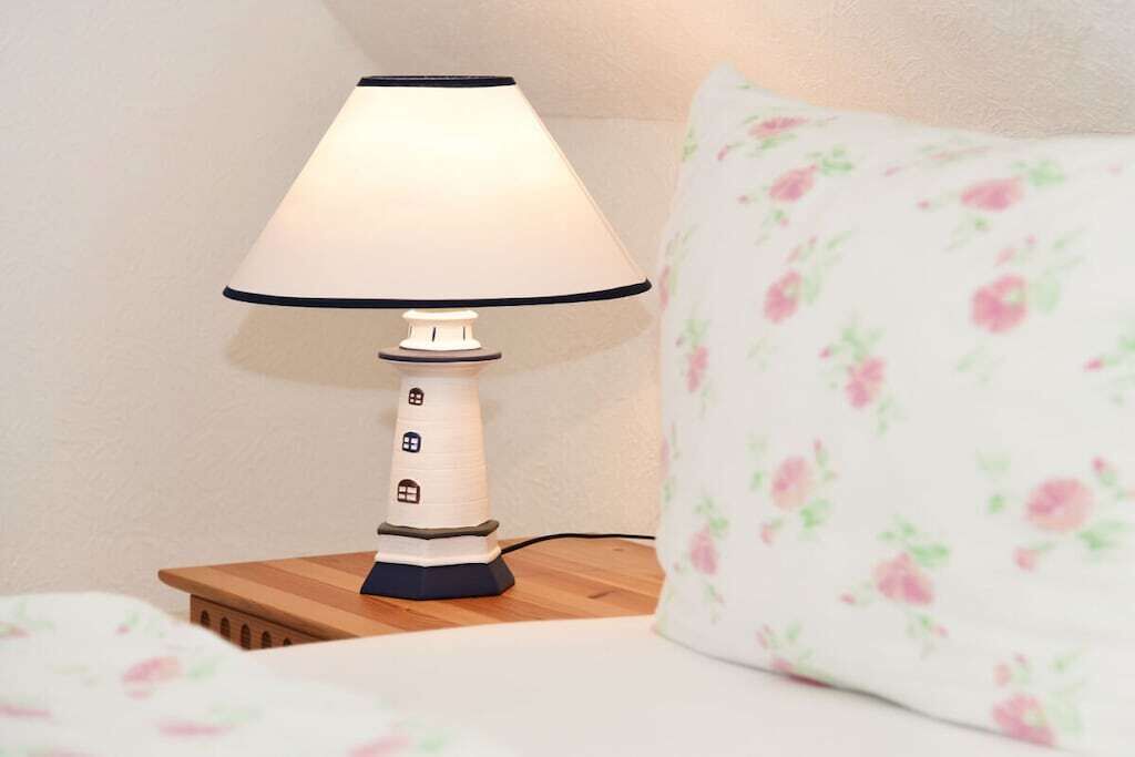 Ein Nachttisch mit Lampe, ein floral gemustertes Kopfkissen und ein Bett mit floraler Bettdecke.
