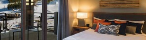 Ein Hotelzimmer mit Bett, Nachttisch mit Lampe und Blick auf eine verschneite Landschaft.
