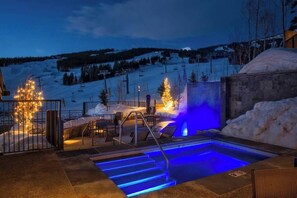 Una piscina esterna riscaldata con gradini per accedervi, circondata da neve e una pista da sci sullo sfondo.