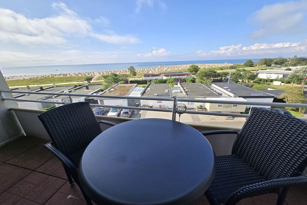 A balcony with a table and chairs, overlooking a beach and parking area.