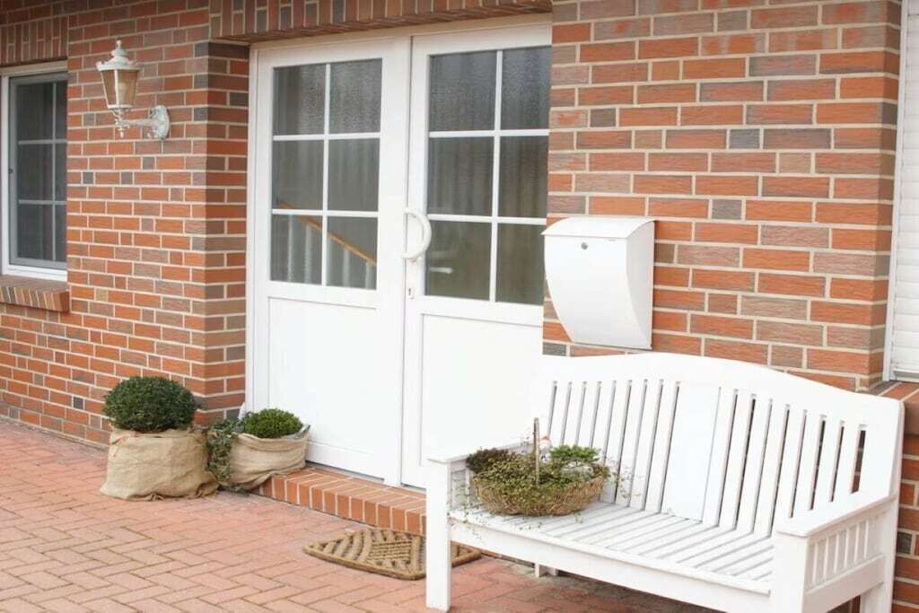 A white bench with a planter, a mailbox, and a door with glass panels.