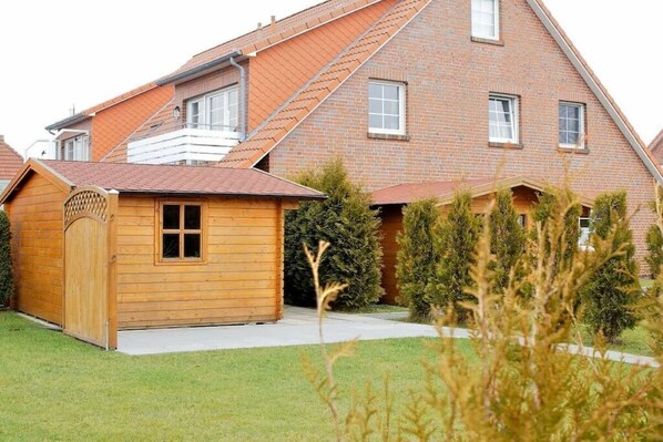 Een tweelaags huis met een schuin dak, een houten tuinhuisje en een verzorgd gazon.
