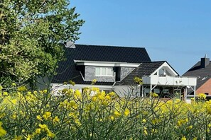 Ein Wohngebäude mit geneigtem Dach, einem sichtbaren Dachboden und einem Vorgarten mit gelb blühenden Pflanzen.