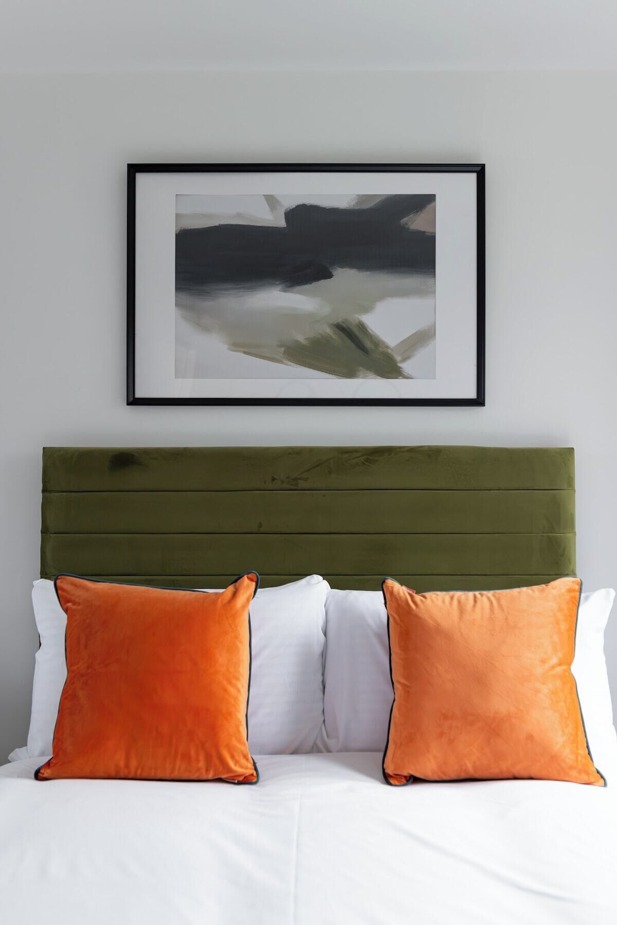 A bed with a green headboard, white bedding, and two orange pillows.
