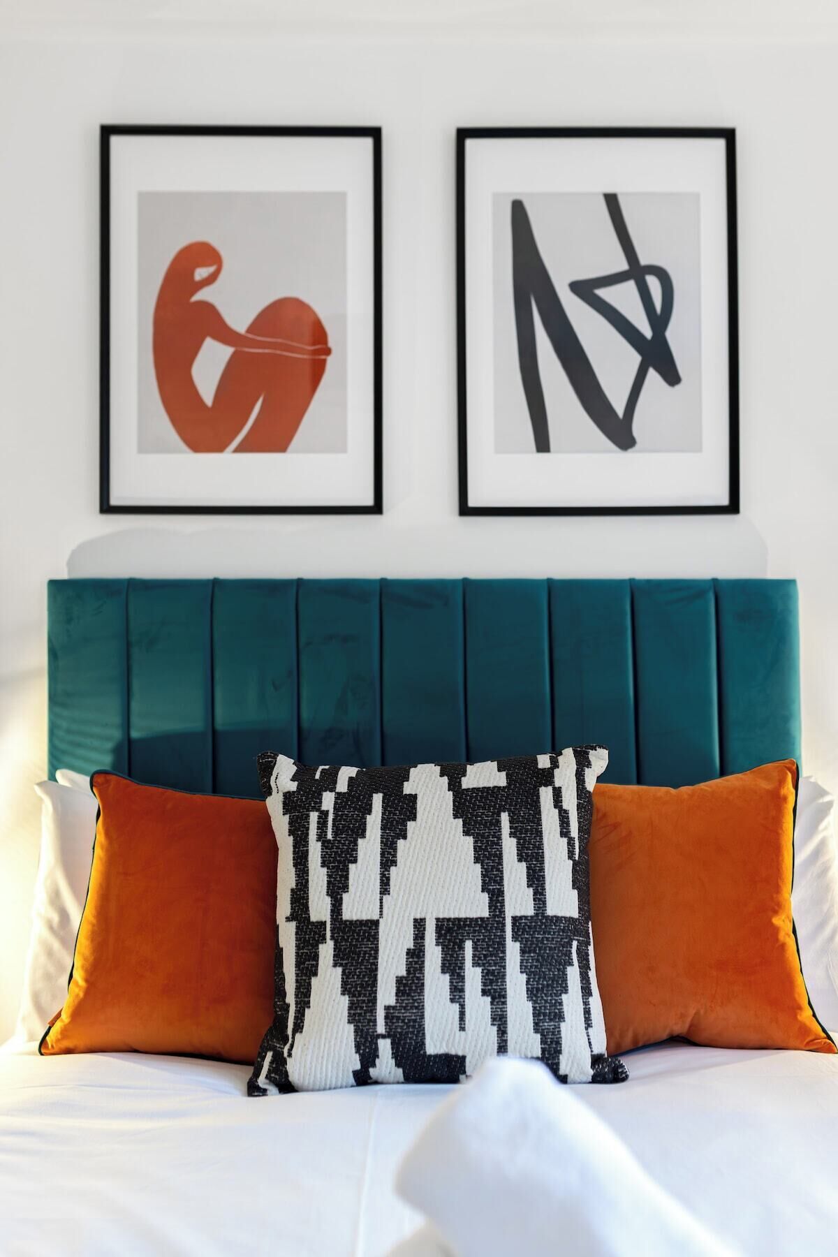 A bed with teal headboard, white bedding, and two orange pillows.