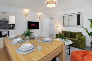Ein moderner Wohnbereich mit Essplatz, einem an der Wand montierten Fernseher und einem grünen Sofa.