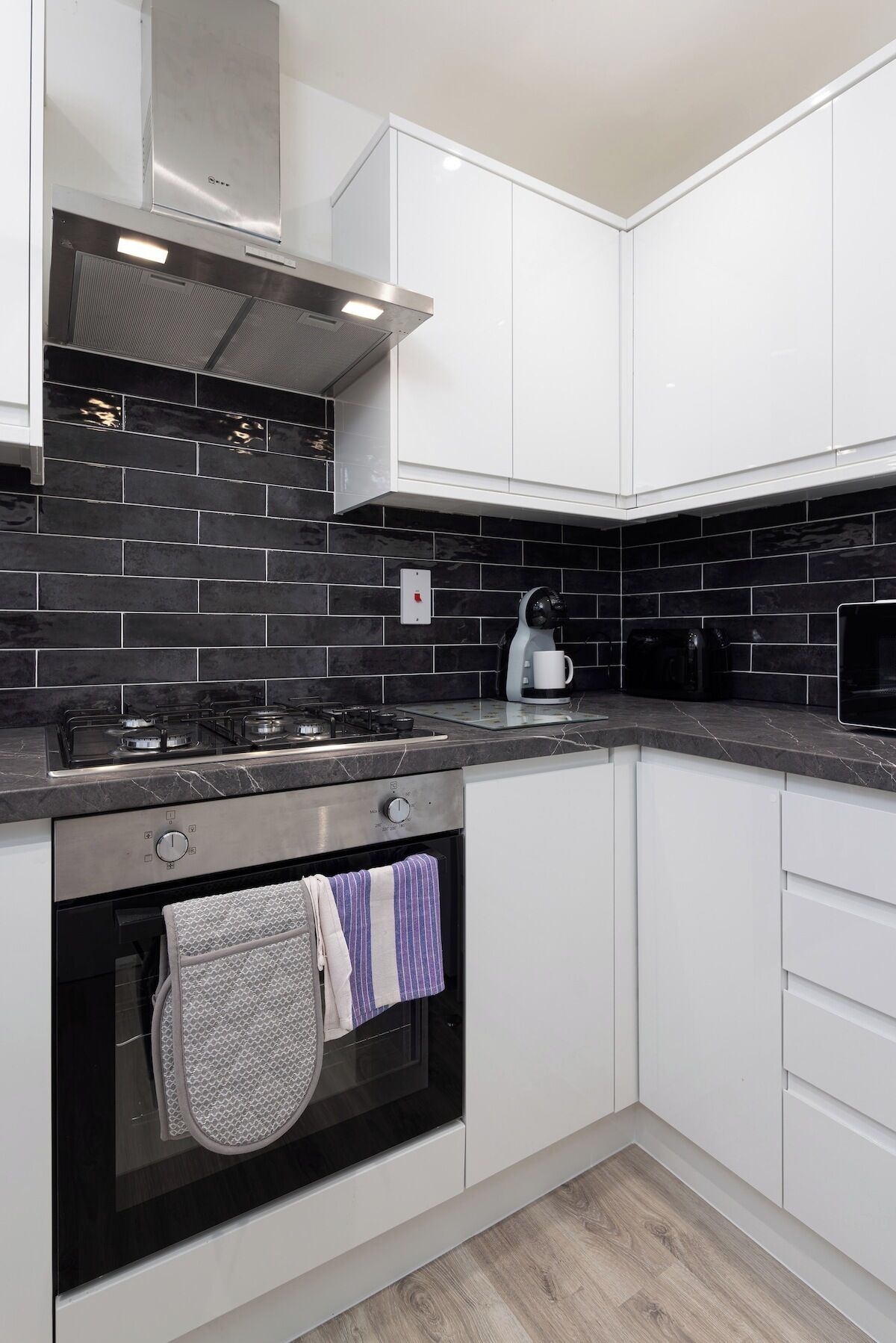 A modern kitchen with white cabinets, a black tiled backsplash, a gas stove, an oven, and a microwave.