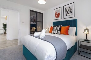 A modern bedroom with a large bed, a nightstand, and a wall-mounted lamp. - Flatzy - Peaceful Sefton Park Luxury Apartment (Liverpool)