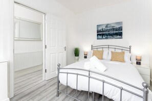 Una camera da letto con struttura letto in metallo, biancheria da letto bianca, un quadro appeso al muro e lampade sui comodini.