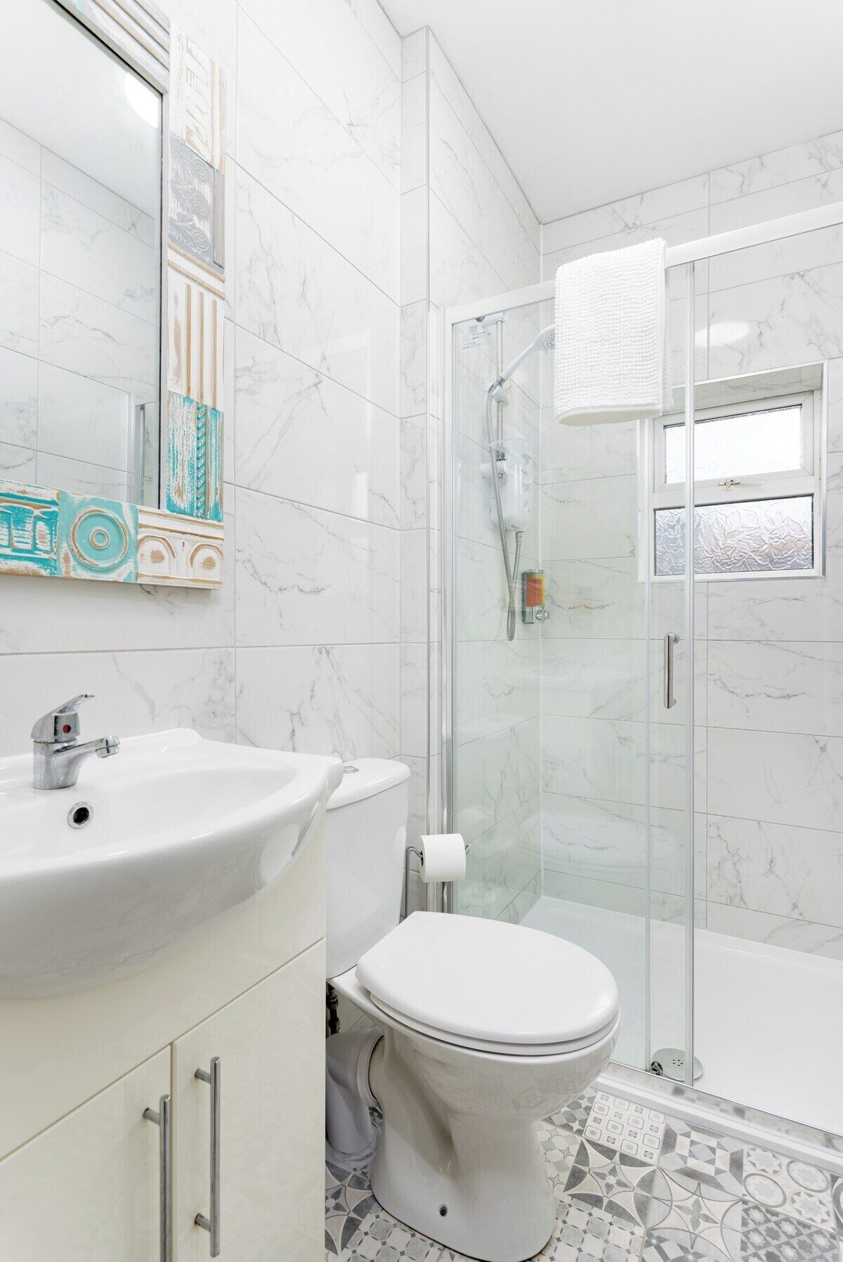 Une salle de bain avec un lavabo blanc, des toilettes et une douche fermée par des parois en verre.