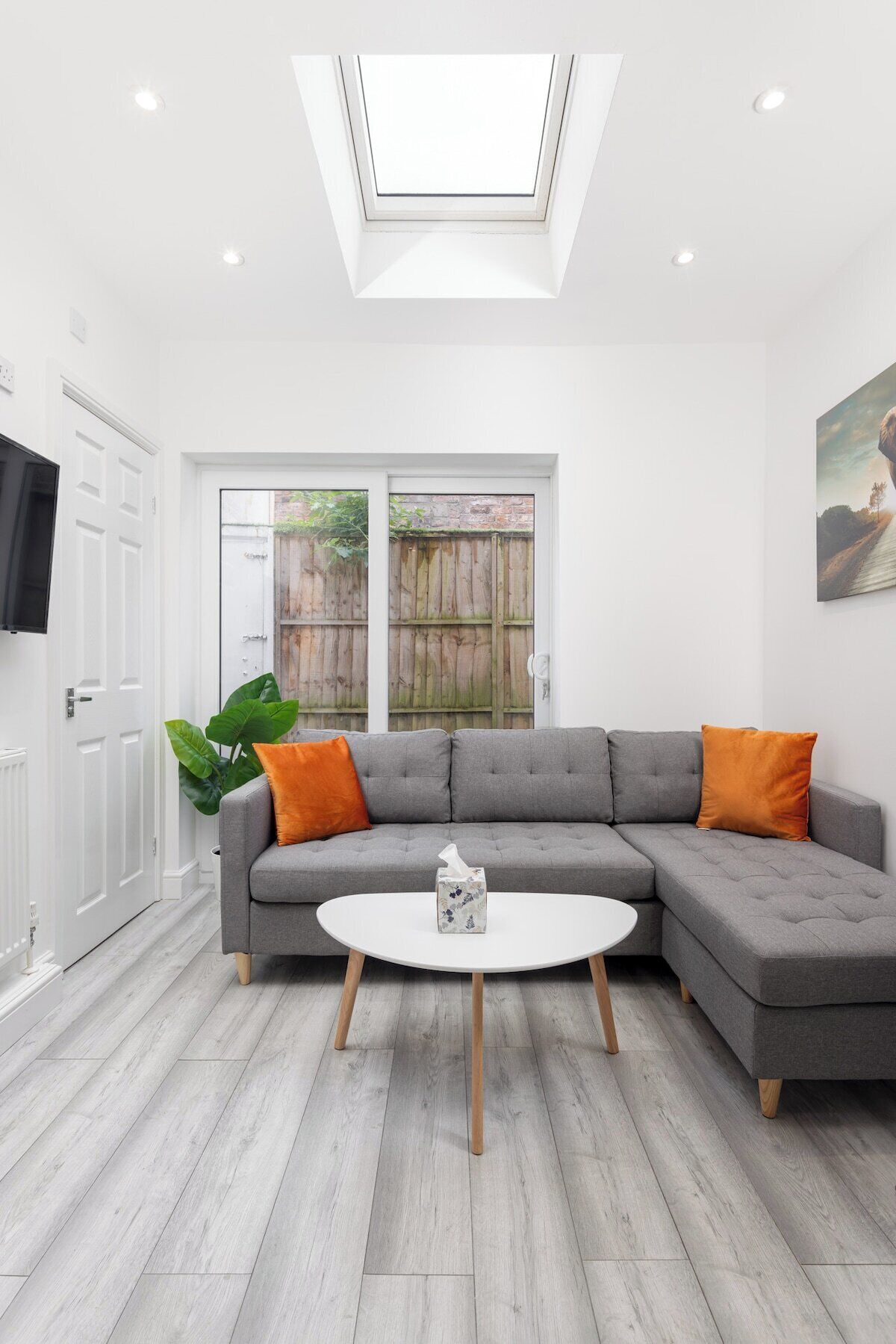 A modern living room with a grey sectional sofa, two orange cushions, a white round coffee table, and a skylight above.