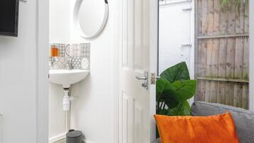 Uma sala de estar moderna com um sofá cinzento, um espelho redondo e uma grande planta verde.