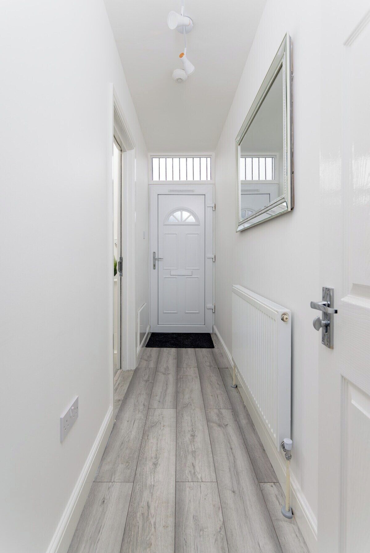 A hallway with a white door, a radiator, and a mirror on the wall.