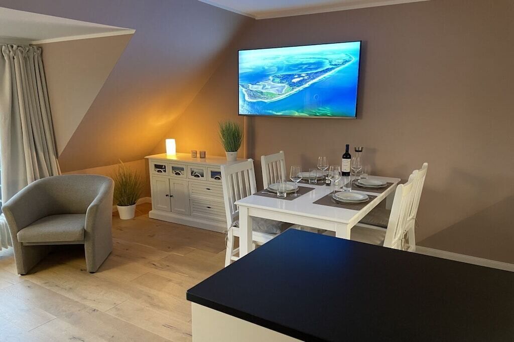 A dining area with a table set for two, a television mounted on the wall, and a potted plant on the sideboard.