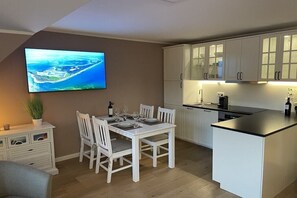 Eine moderne Küche mit weißen Schränken, einem Esstisch für vier Personen und einem an der Wand befestigten Flachbildfernseher.