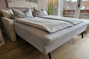 Ett modernt sovrum med en stor säng, en soffa och utsikt över en byggnad genom en glasdörr.