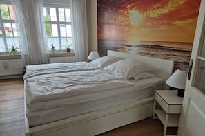A bedroom with a bed, bedside lamps, a window with curtains, and a wall with a sunset painting. - Holiday apartment in Lemgo with swimming pool (Lemgo)