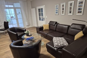A modern living room with a leather sofa, a glass coffee table, and a chair. There are framed pictures on the wall and a door leading to a balcony. - Holiday apartment in Lemgo with swimming pool (Lemgo)