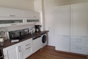 Cuina amb armaris blancs, rentaplats, cafetera i rentadora.