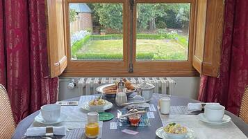 Une table à manger dressée pour le petit-déjeuner, avec vue sur un jardin par la fenêtre.
